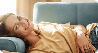 Imagem de mulher com camiseta amarela deitada no sofá e sorrindo.